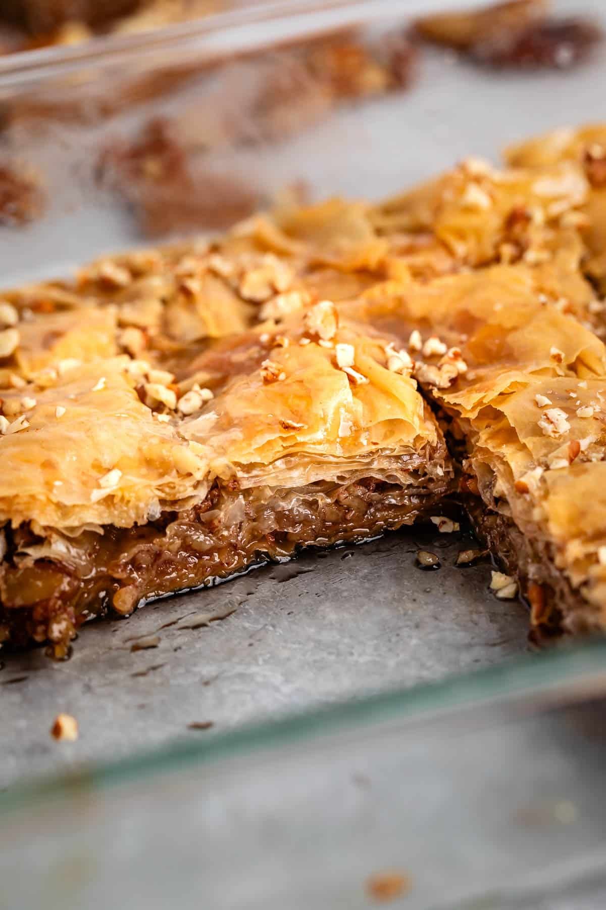 pecan baklava laying in a glass pan with pecans layered in the baklava.