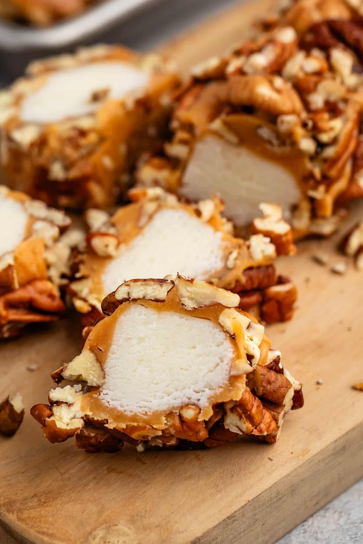 sliced pecan logs covered in caramel and pecans on a cutting board.