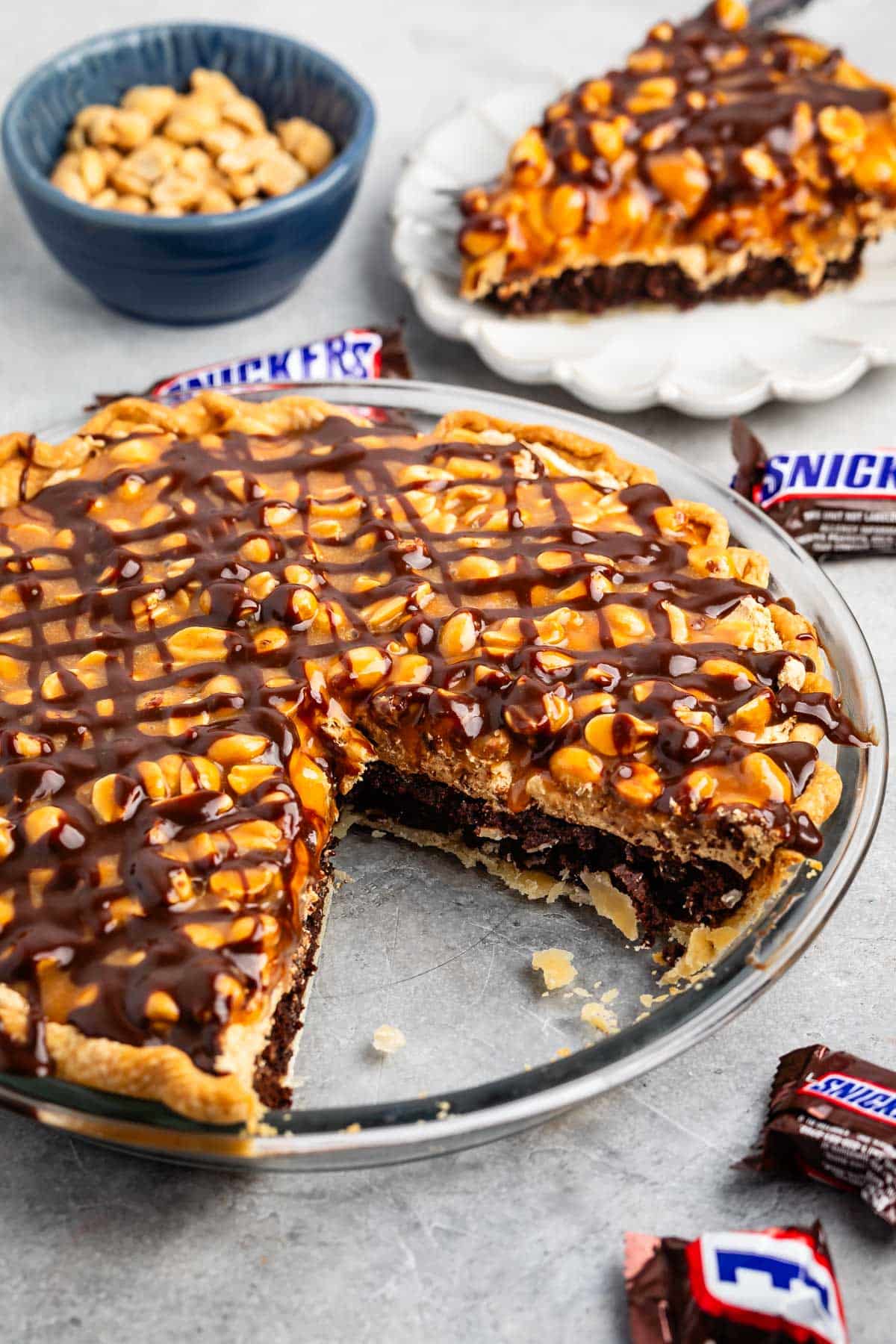 sliced snickers pie with nuts and chocolate sauce on top.