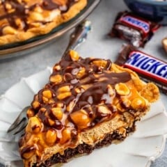 sliced snickers pie with nuts and chocolate sauce on top.