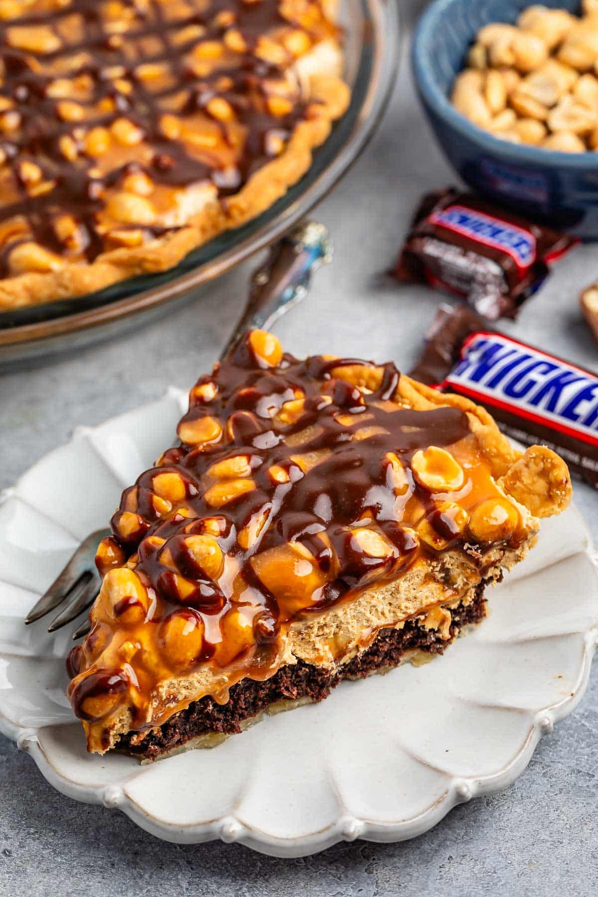 sliced snickers pie with nuts and chocolate sauce on top.
