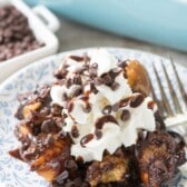 French toast mixed with many chocolate chips in a white dish with whipped cream on top.