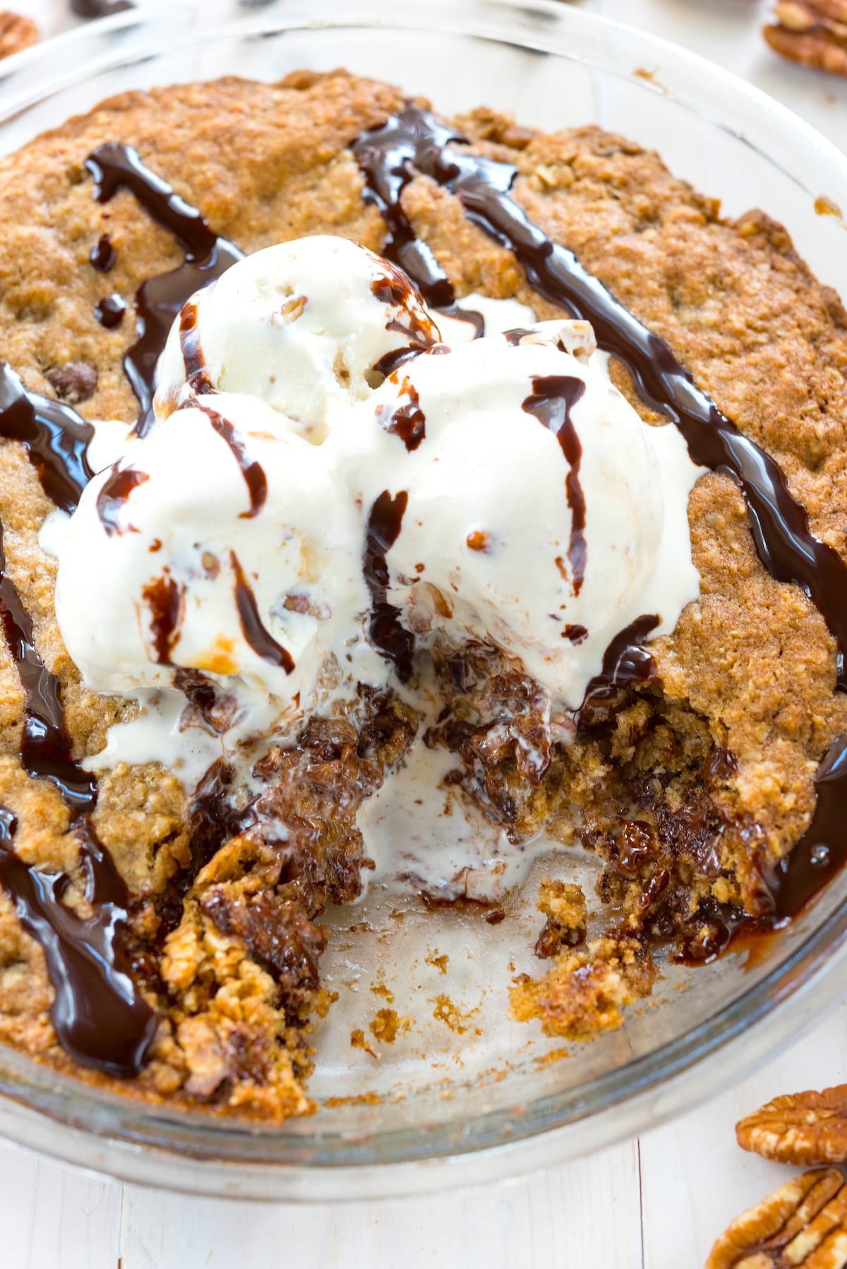 oatmeal cookie in pie plate with ice cream and chocolate sauce an slice missing.