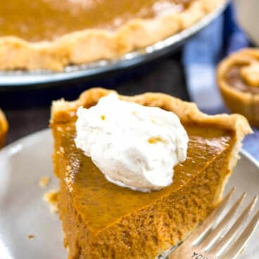 one triangle slice of pumpkin pie with a dollop of whipped cream on a white plate.