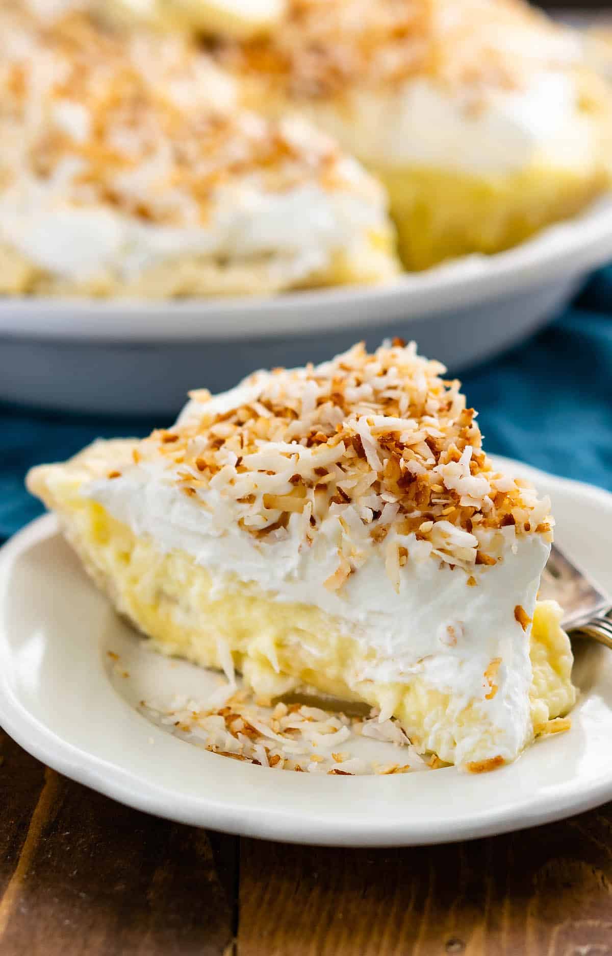 one triangle slice of banana cream pie topped with shredded coconut on a white plate.