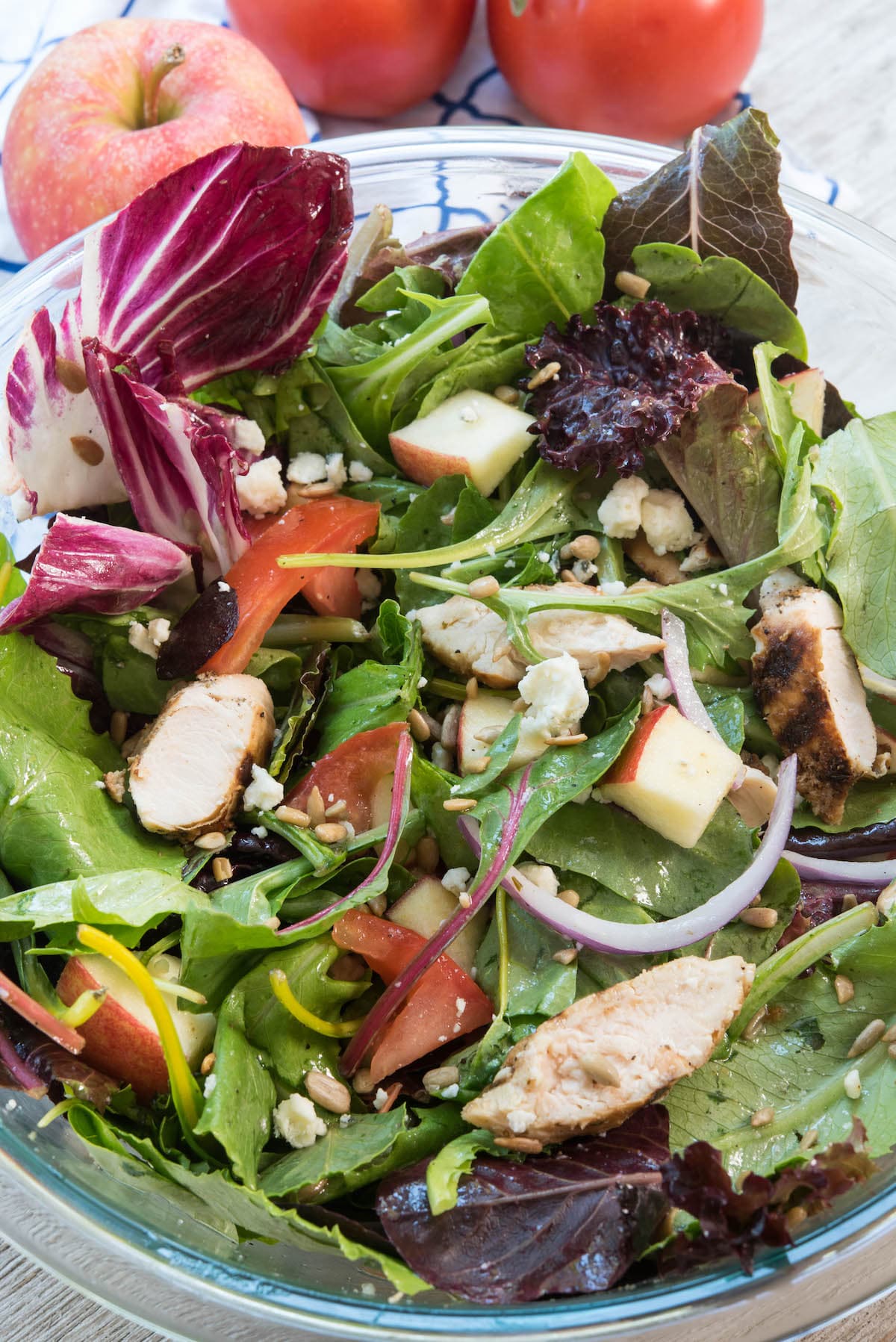 salad mixed with apples and onions and chicken and more in a clear bowl.