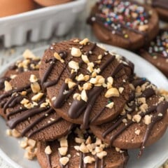 stacked chocolate cookies on a white plate with chocolate drizzled over top.