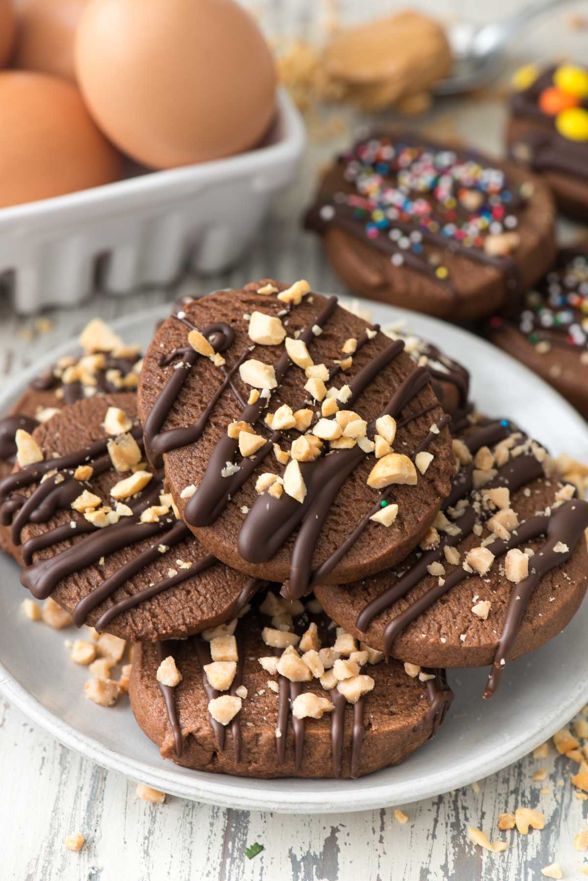 stacked chocolate cookies on a white plate with chocolate drizzled over top.