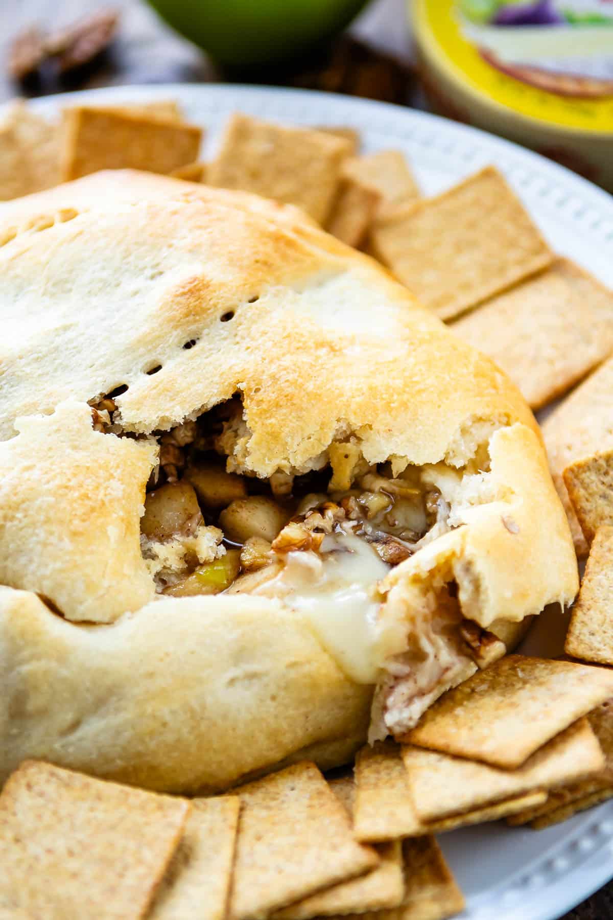 crackers surrounding baked brie that's covered with dough on a white plate.