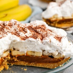 pie layered with graham cracker crust and chocolate and bananas and whipped cream in a clear pan.