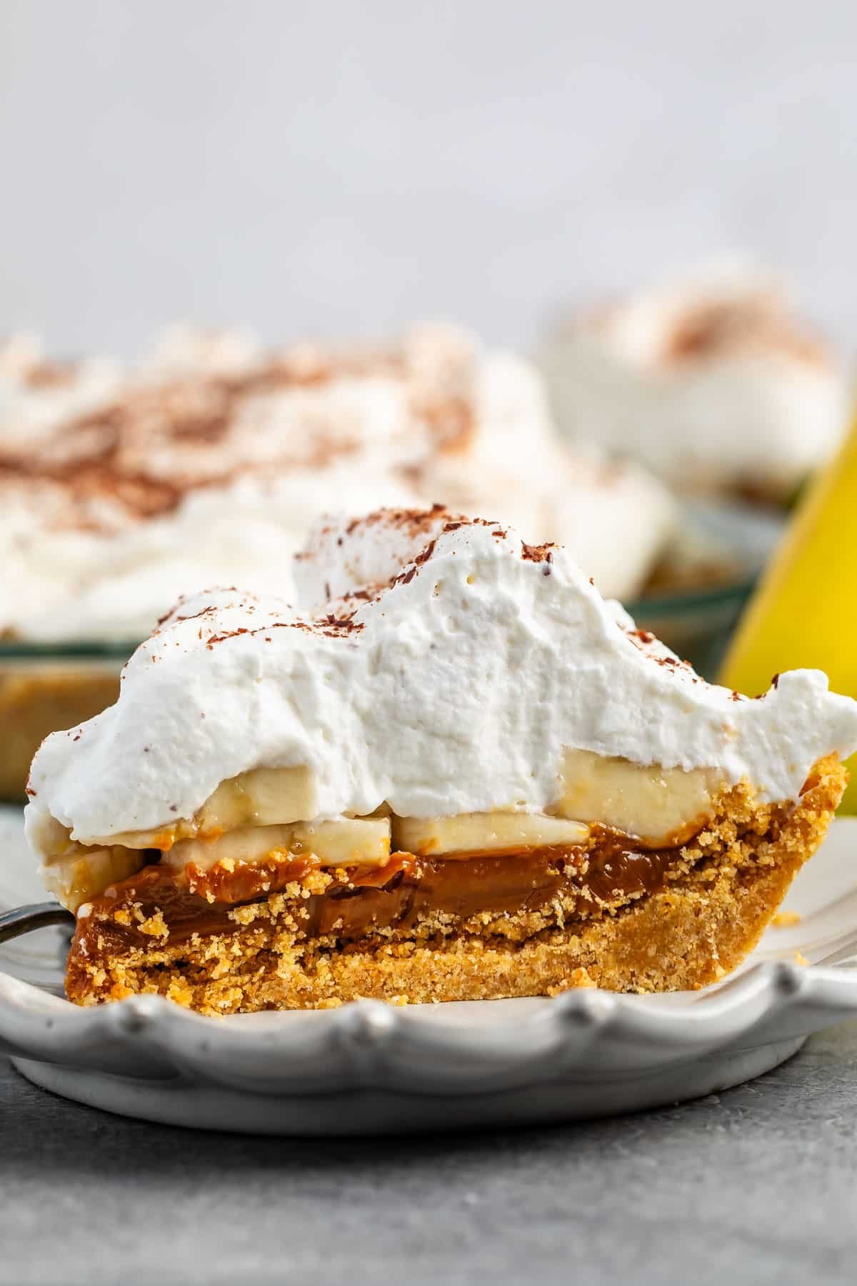 pie layered with graham cracker crust and chocolate and bananas and whipped cream on a white plate.