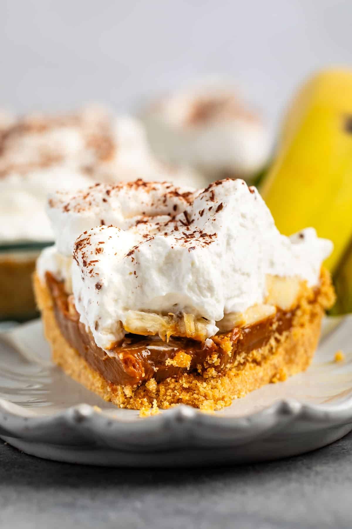 pie layered with graham cracker crust and chocolate and bananas and whipped cream on a white plate.