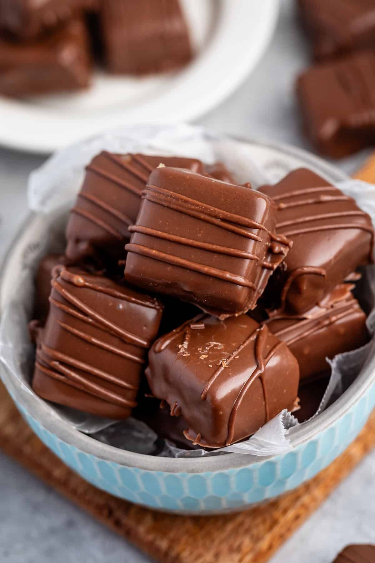 stacked butterscotch squares covered in chocolate in a light blue bowl.