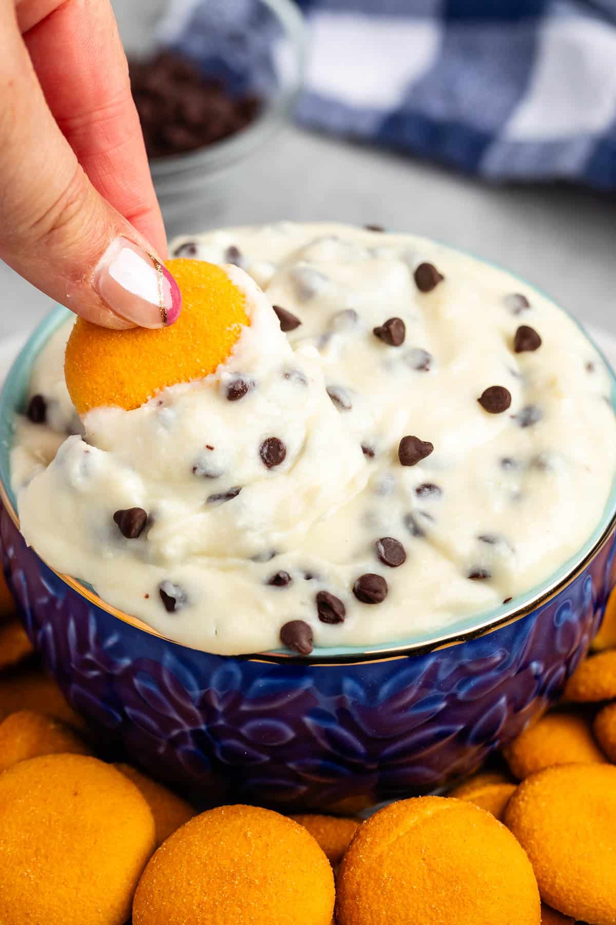 cannoli dip in a blue bowl with orange cookie wafers next to the bowl and hand dipping cookie into the bowl.