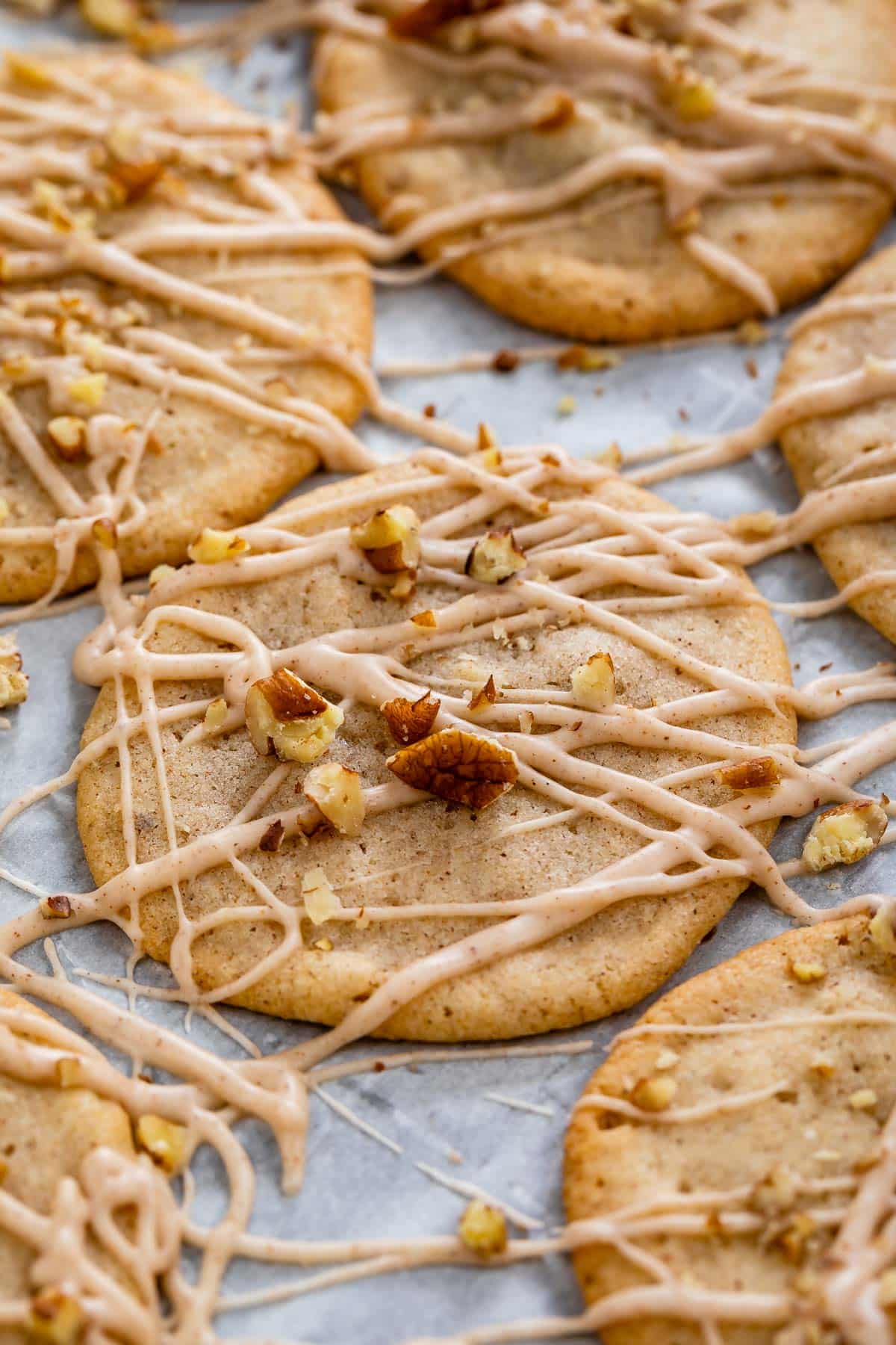 cookies laid out on parchment paper with icing and chopped pecans sprinkled over top.