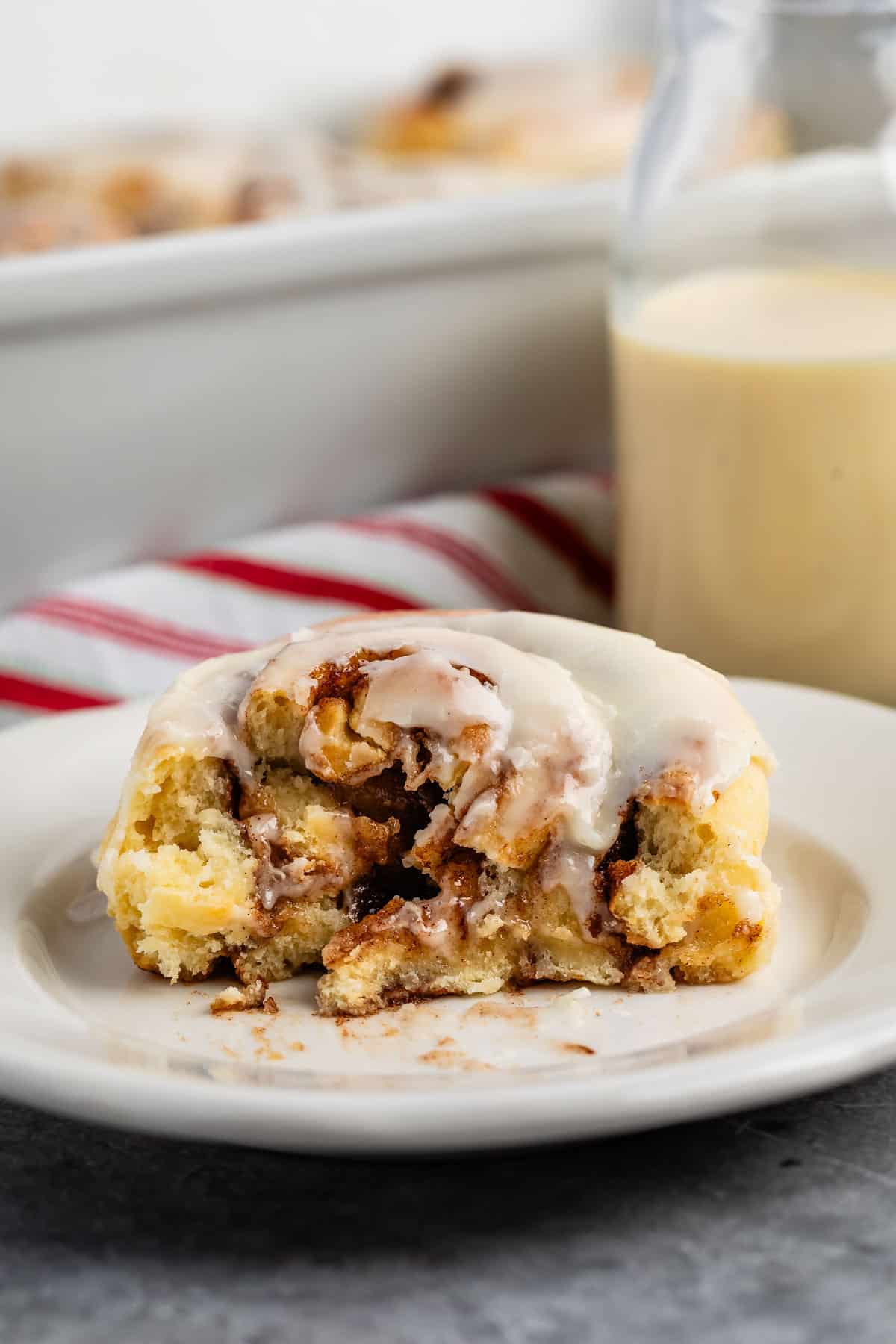 cinnamon roll on a white plate with eggnog in the background.