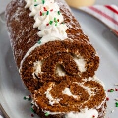 sliced gingerbread cake roll with whipped cream and sprinkles on top on a grey plate.