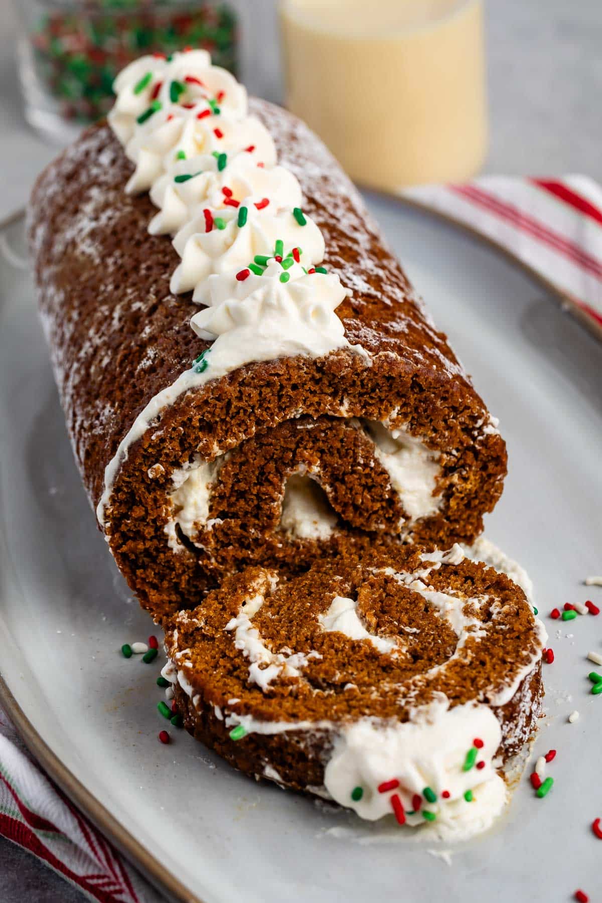 sliced gingerbread cake roll with whipped cream and sprinkles on top on a grey plate.