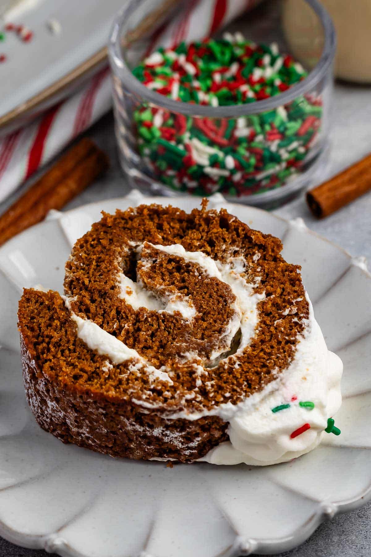 sliced gingerbread cake roll with whipped cream and sprinkles on top on a grey plate.