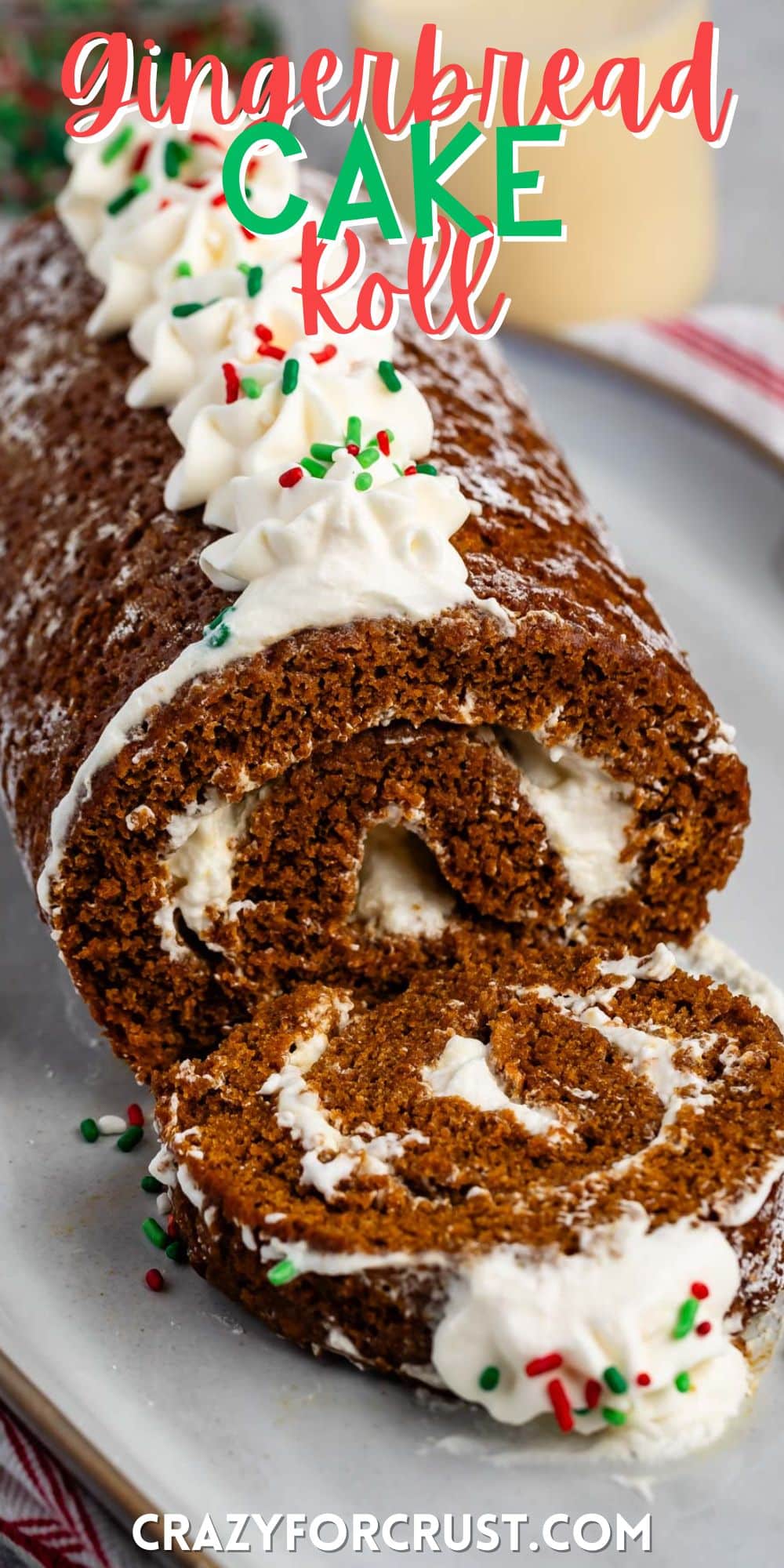 sliced gingerbread cake roll with whipped cream and sprinkles on top on a grey plate with words on the image.