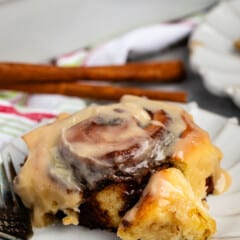 cinnamon roll on a grey plate with icing in top.