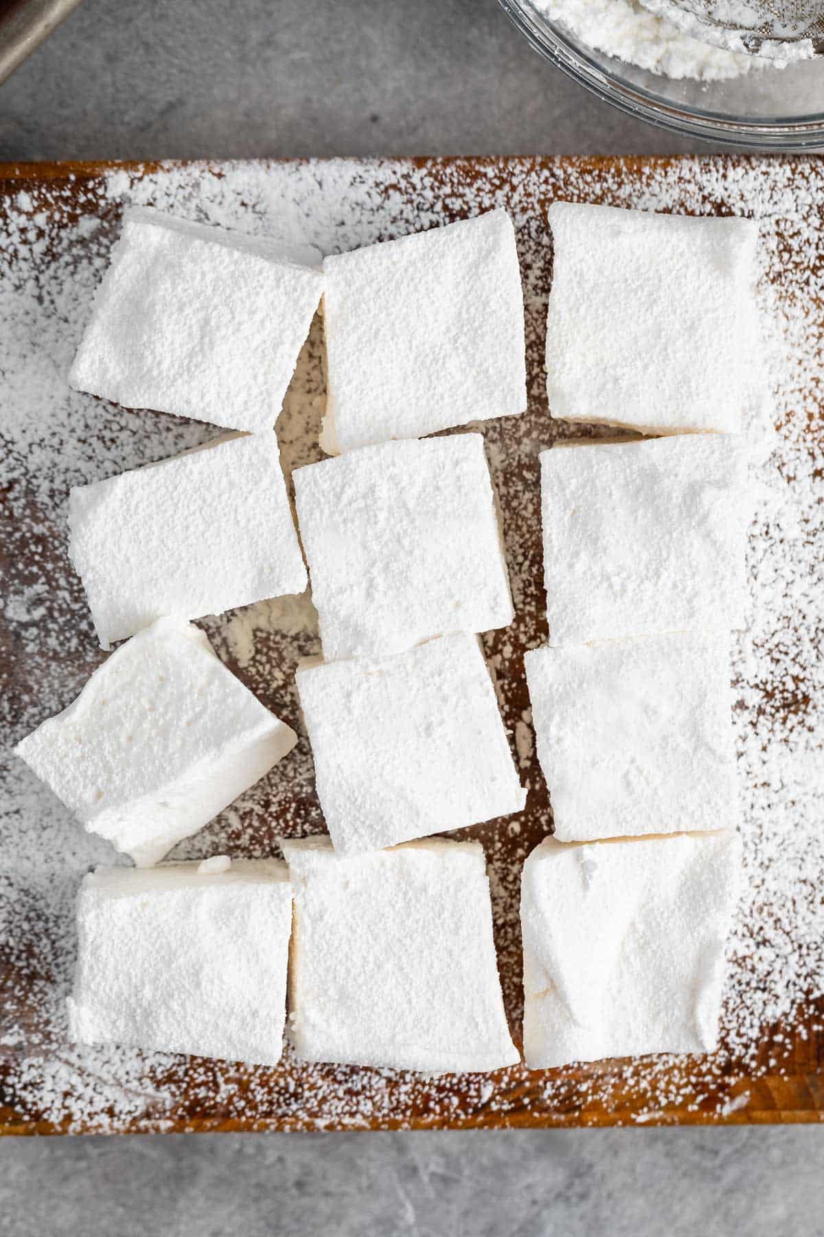 large homemade marshmallows laid on top of powdered sugar on a cutting board.