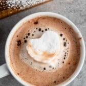 heart shaped marshmallow floating in hot chocolate in a white mug.