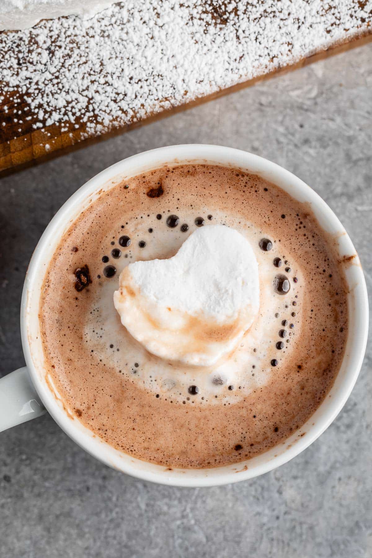 heart shaped marshmallow floating in hot chocolate in a white mug.