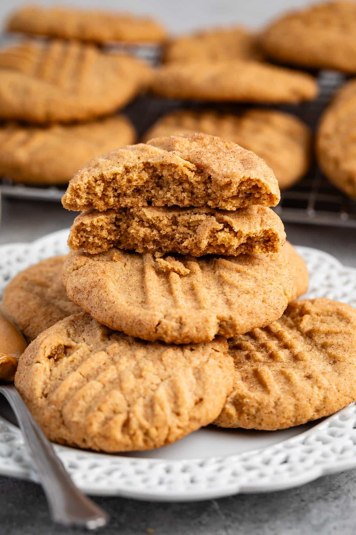 stacked peanut butter snickerdoodles on a white plate next to a spoonful of peanut butter.