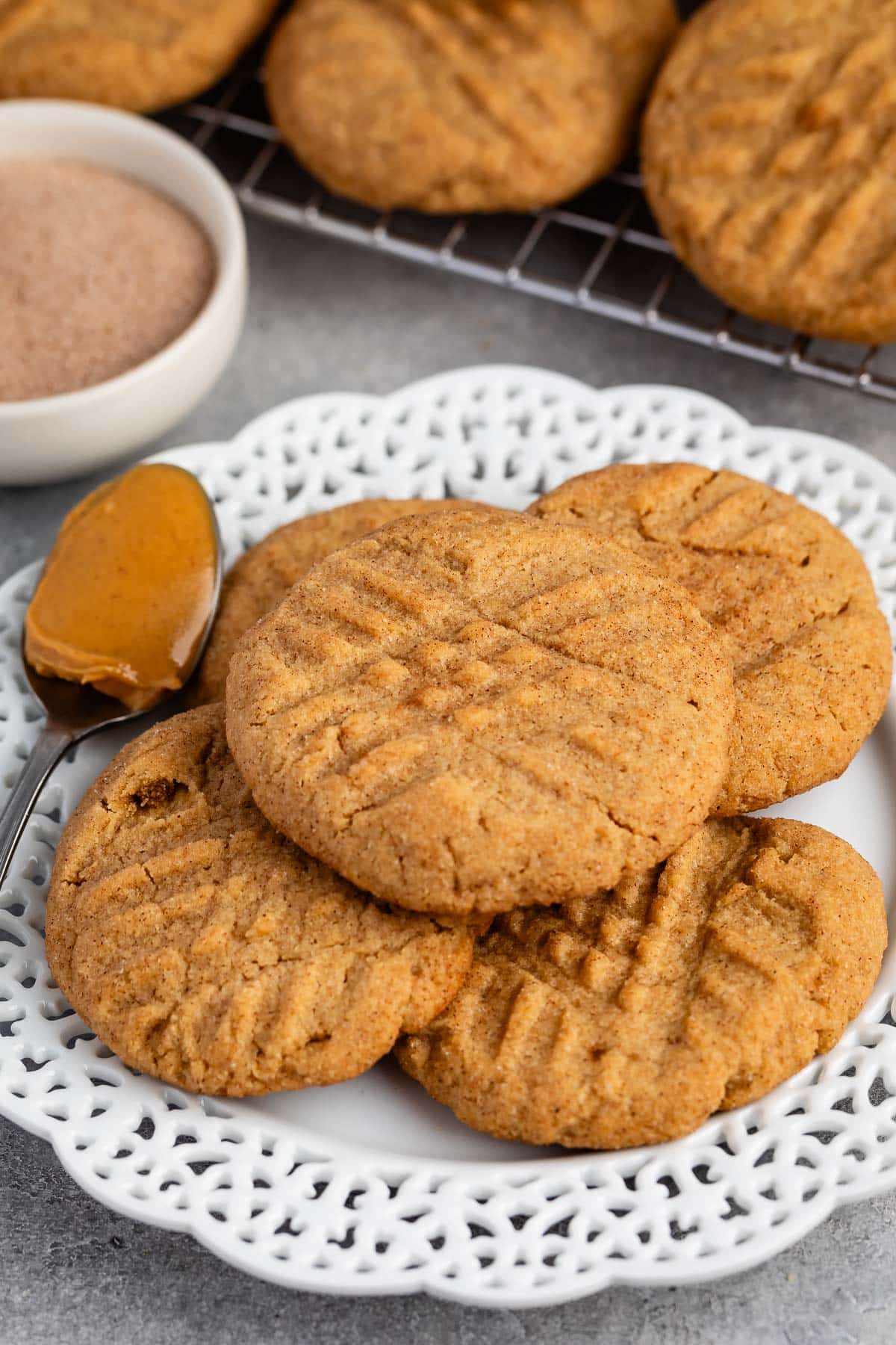 stacked peanut butter snickerdoodles on a white plate next to a spoonful of peanut butter.