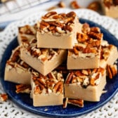stacked pecan fudge with chopped pecan pressed on top on a blue plate.