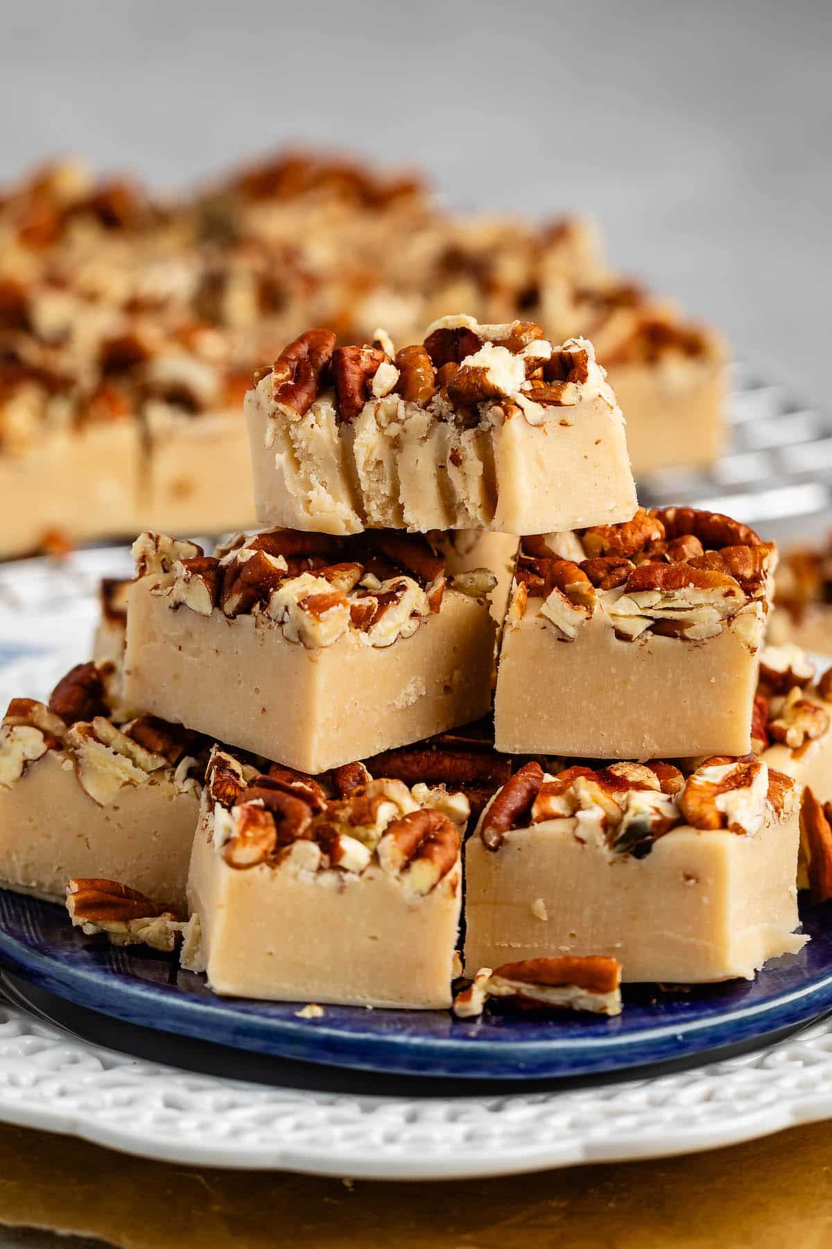 stacked pecan fudge with chopped pecan pressed on top on a blue plate.