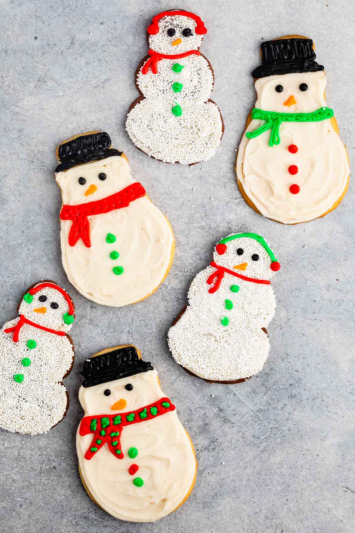 snowman cookies covered in white frosting and sprinkles and icing to replicate a snowman.