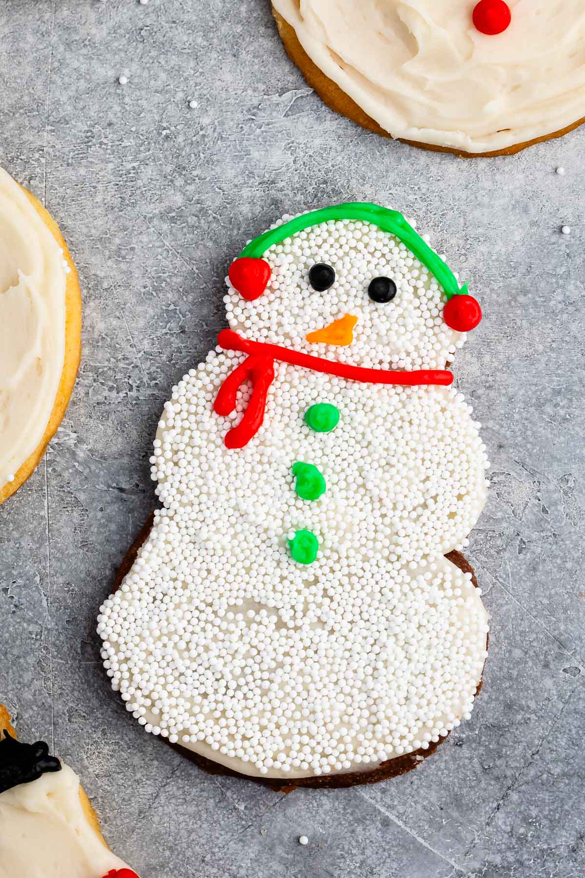 snowman cookies covered in white frosting and sprinkles and icing to replicate a snowman.