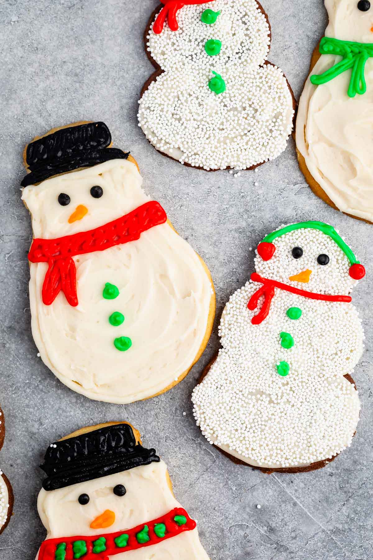 snowman cookies covered in white frosting and sprinkles and icing to replicate a snowman.