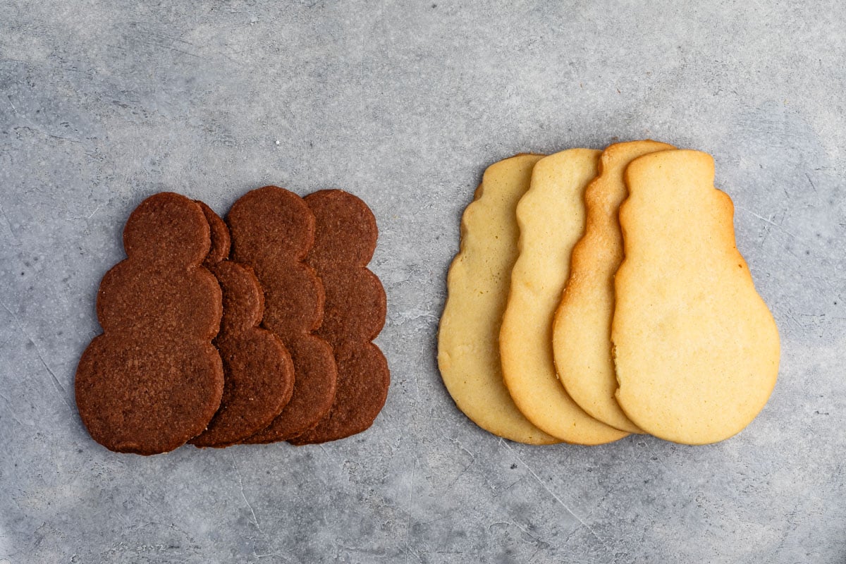 regular and chocolate snowman shaped cookies stacked with no frosting on them.