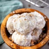 stacked snowballs covered in powdered sugar in a wood bowl.