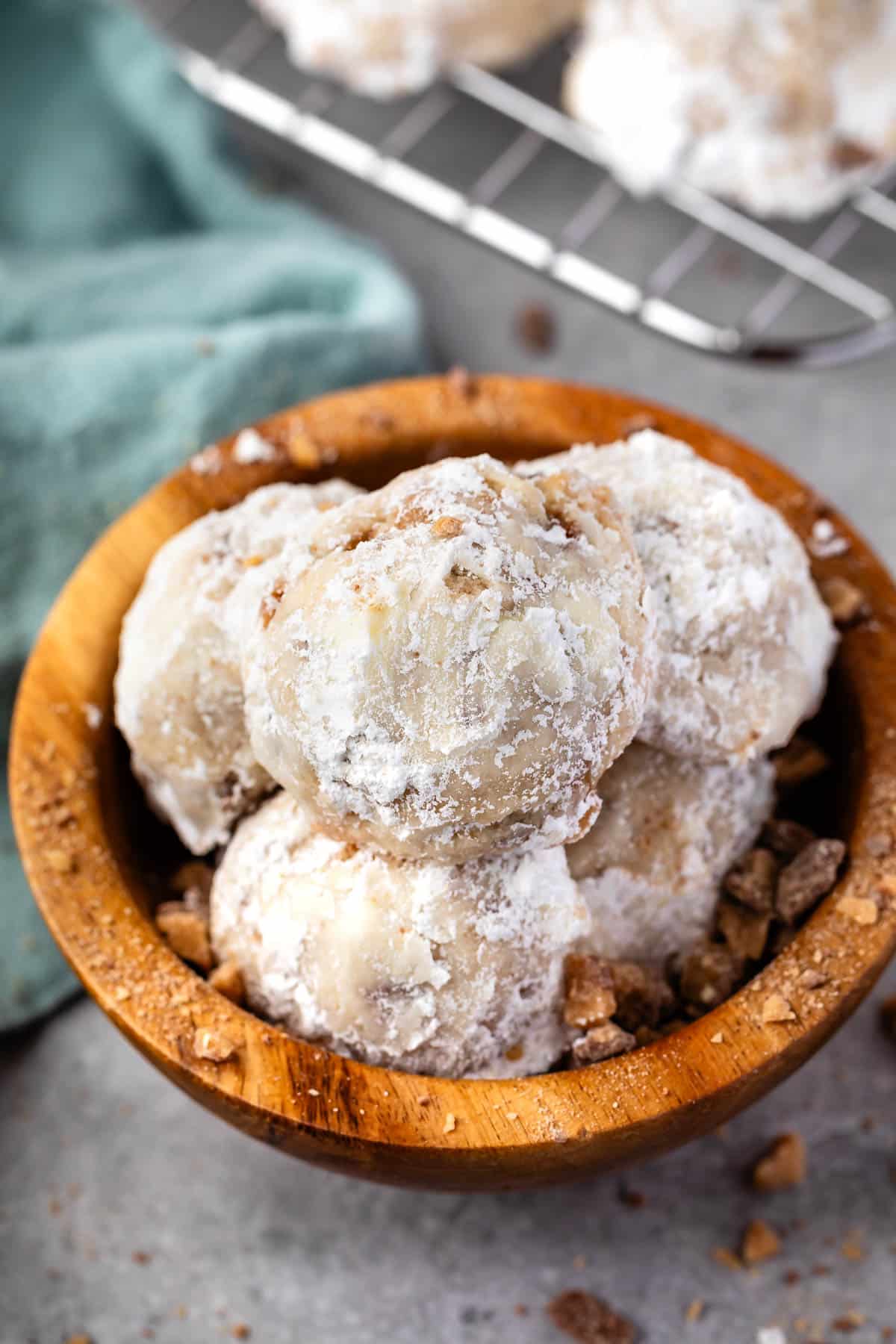 stacked snowballs covered in powdered sugar in a wood bowl.