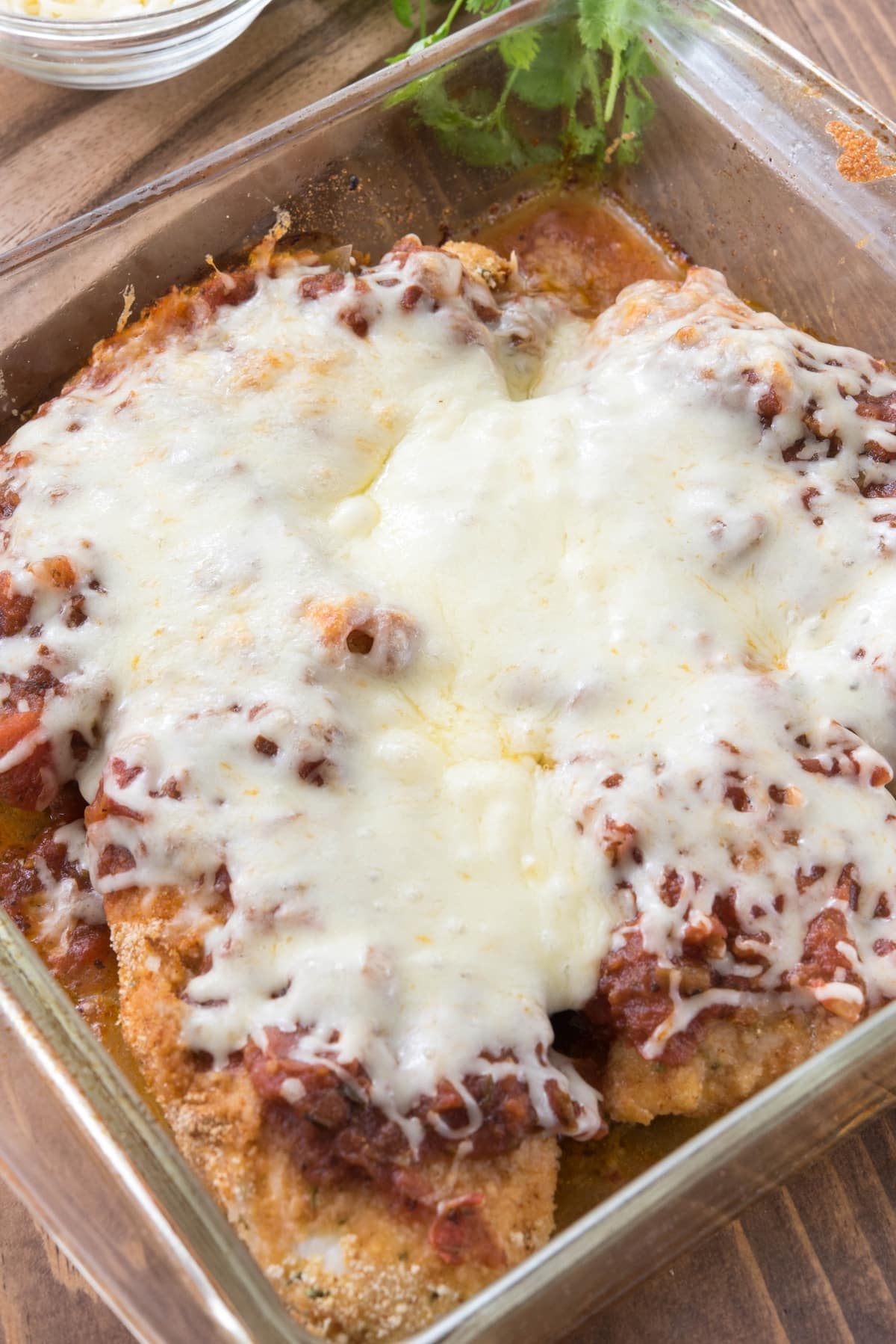 chicken breasts covered in sauce and cheese in a glass pan.