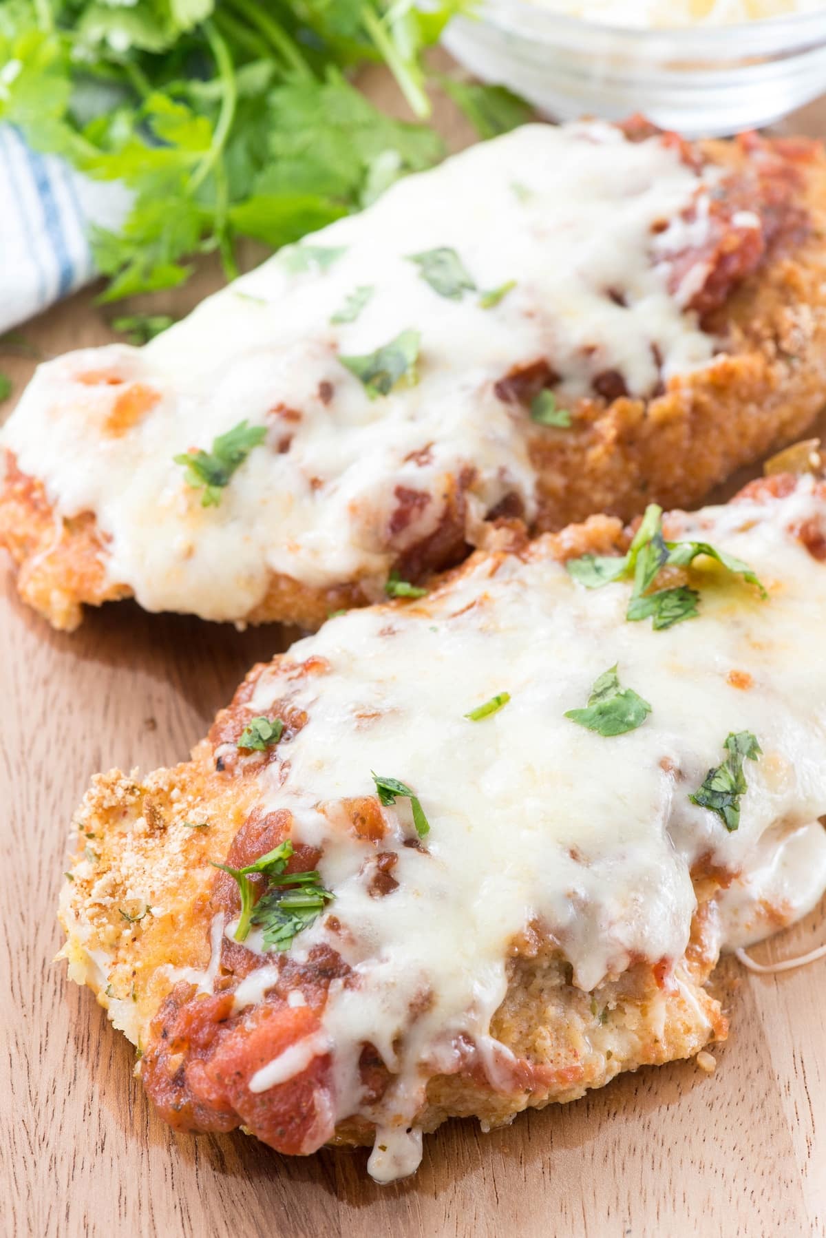 chicken breasts covered in sauce and cheese on a cutting board.