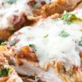 chicken breasts covered in sauce and cheese on a cutting board.