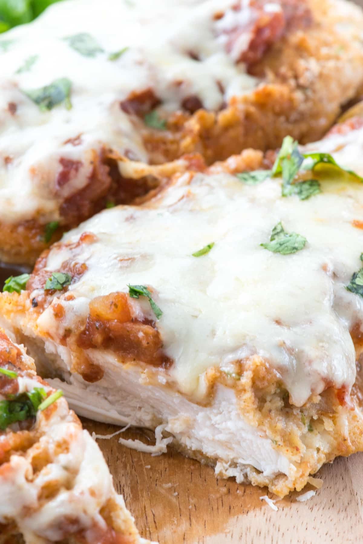 chicken breasts covered in sauce and cheese on a cutting board.