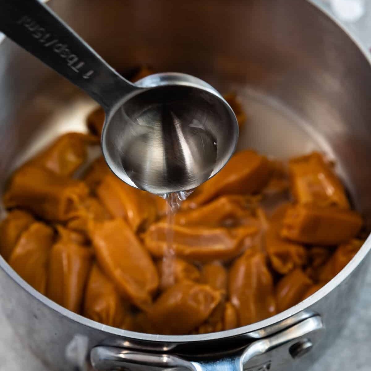 tablespoon pouring water into pan of caramels.