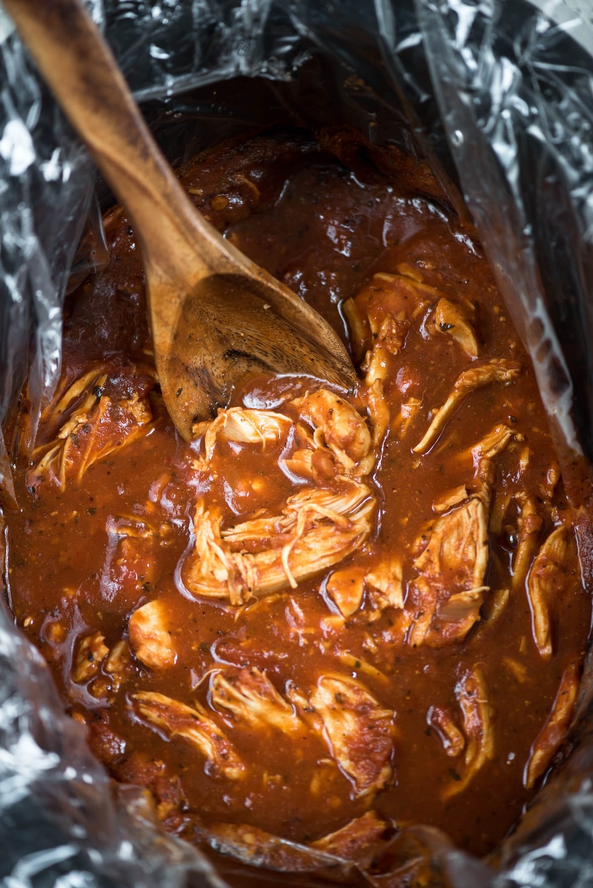 chicken marinara in a black crockpot with a wooden spoon stirring the dinner.