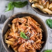 chicken marinara mixed quirk pasta in a brown bowl with cheese sprinkles on top.