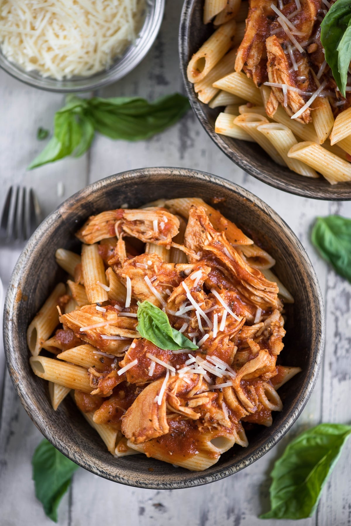 chicken marinara mixed quirk pasta in a brown bowl with cheese sprinkles on top.