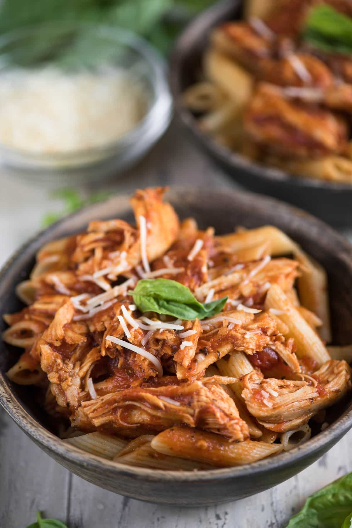 chicken marinara mixed quirk pasta in a brown bowl with cheese sprinkles on top.