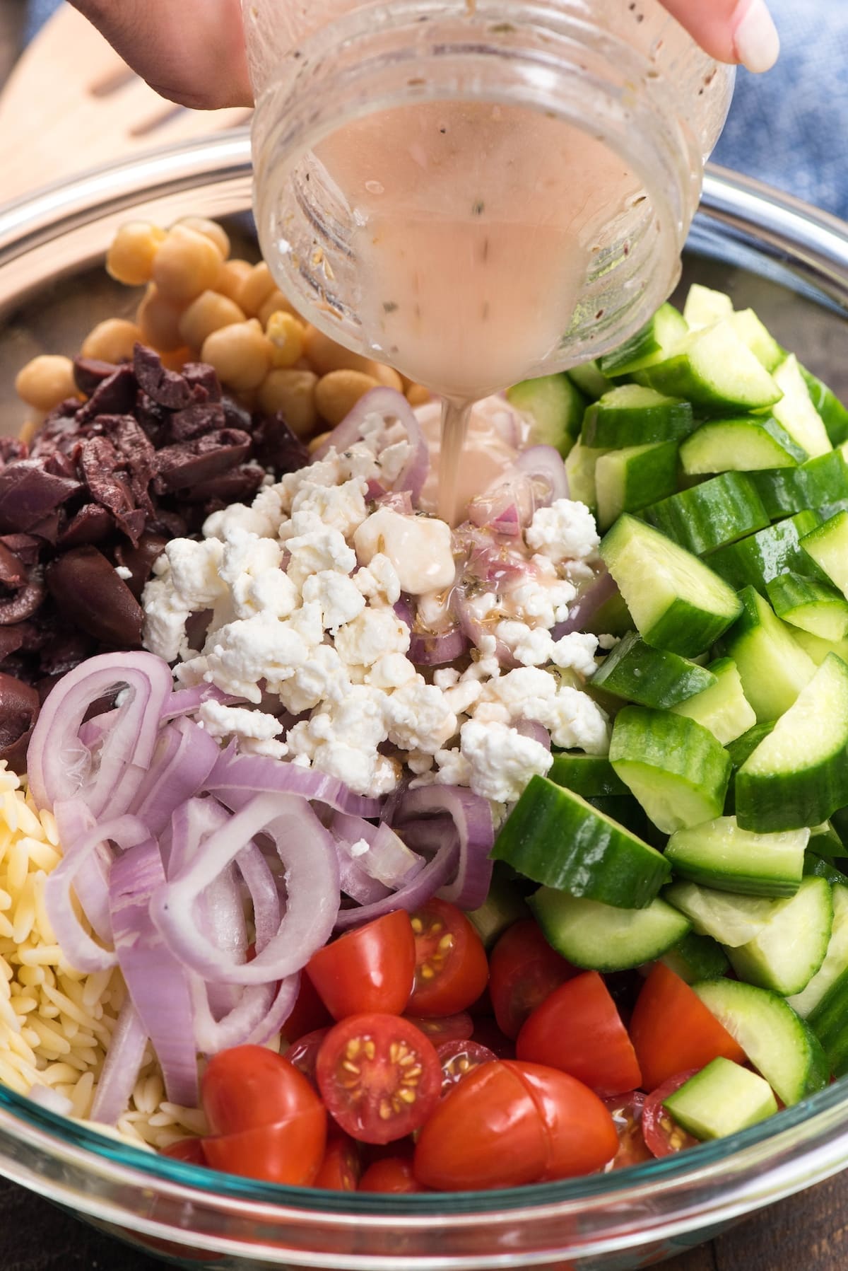 salad mixed together with dressing being poured in, in a clear bowl.