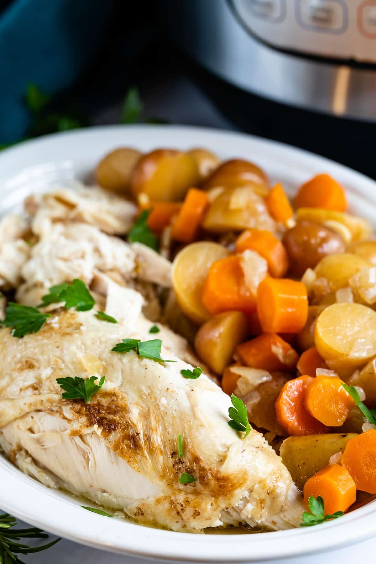chicken and carrots and potatoes in a white bowl with an instant pot in the back.