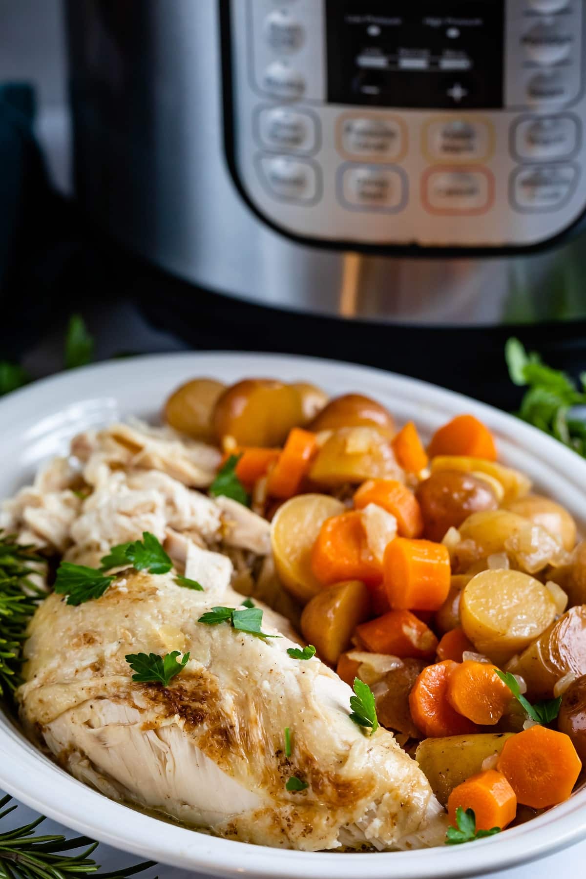 chicken and carrots and potatoes in a white bowl with an instant pot in the back.